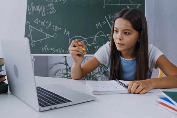 kid studying while looking at laptop and writing on notebook