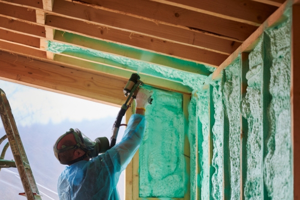 Worker spraying polyurethane foam for insulating wall and ceiling