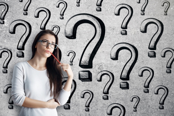 woman holding a pen against her cheek standing by a wall of question marks depicting FAQs about retrofitting insulation