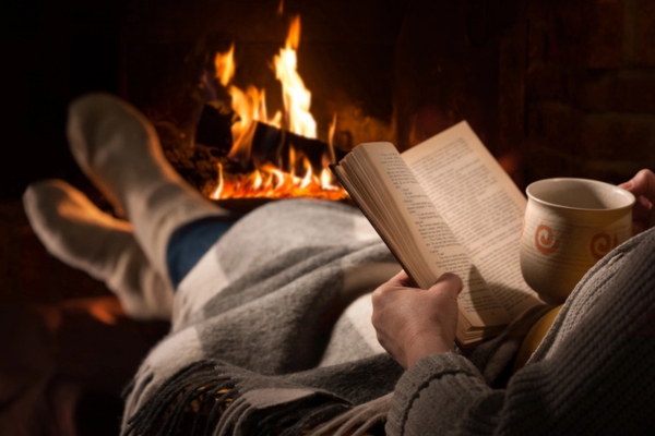 woman staying cozy and warm by the fireplace while reading a book and drinking hot cocoa depicting importance of proper insulation